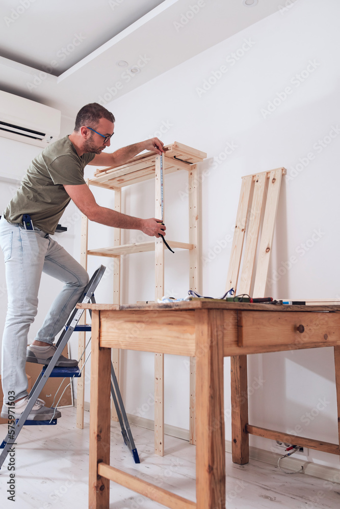 Man assembling new wooden shelf and furniture in the apartment.