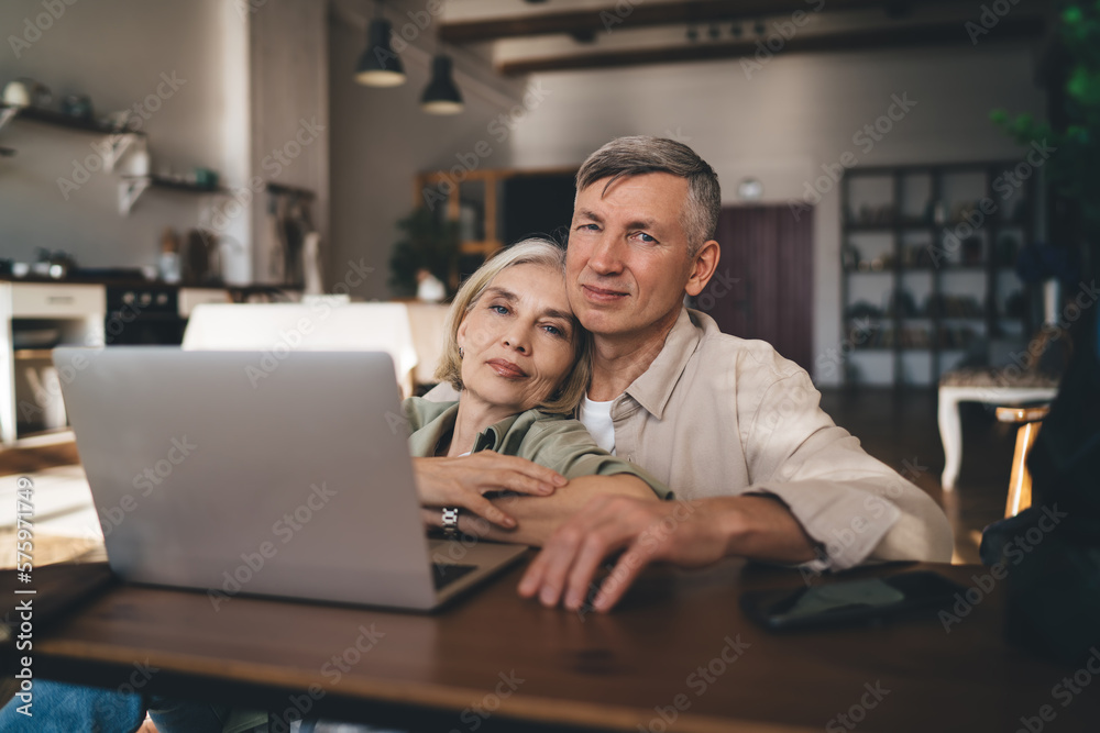 Happy aged man embracing woman while sitting at coffee table with laptop Happy aged man embracing woman while sitting at coffee table with laptop