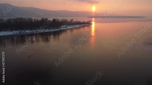 View of the hills by the river at sunset. Orange sun over my river. Snow lies on the island. Top view from a drone.
