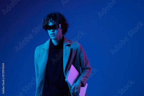Portrait of a male hacker with a laptop and futuristic glasses in blue light, Blue Perennial color, cyber security, technology, laptop copy space, template, trendy neon, freelance online work