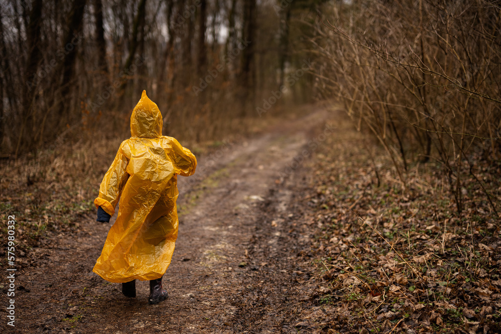 Rear view of boy in yellow raincoat walking in the forest after rain. Rear view of boy in yellow raincoat walking in the forest after rain.