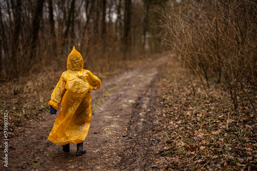 Obraz na plátně Rear view of boy in yellow raincoat walking in the forest after rain