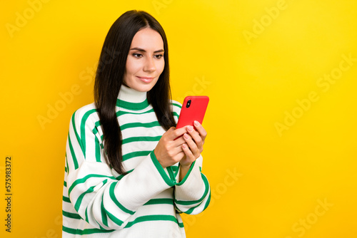 Photo of pretty sweet woman wear striped sweater communicating modern device empty space isolated yellow color background