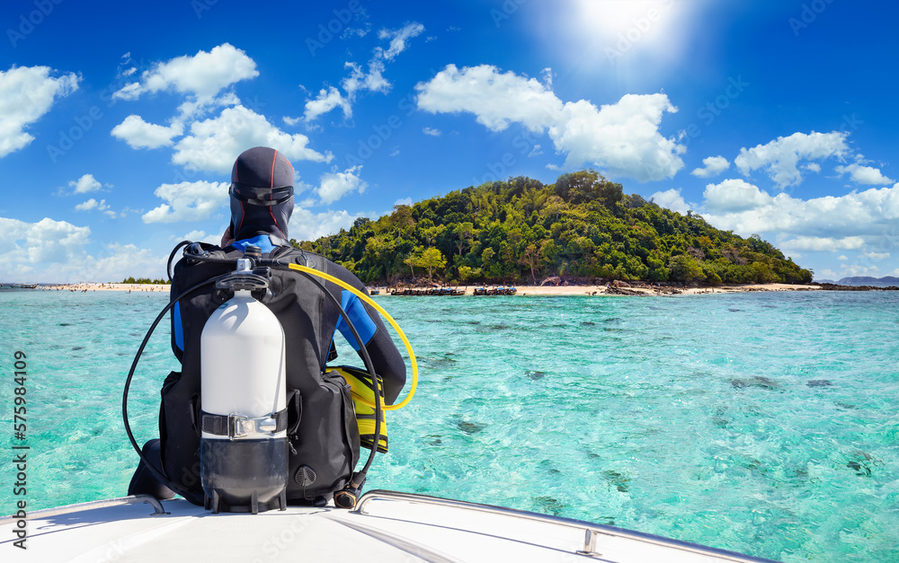 A scuba diver in his diving gear sits in front of a boat and enjoys the view of the tropical landscape with turquoise sea in Krabi, Thailand