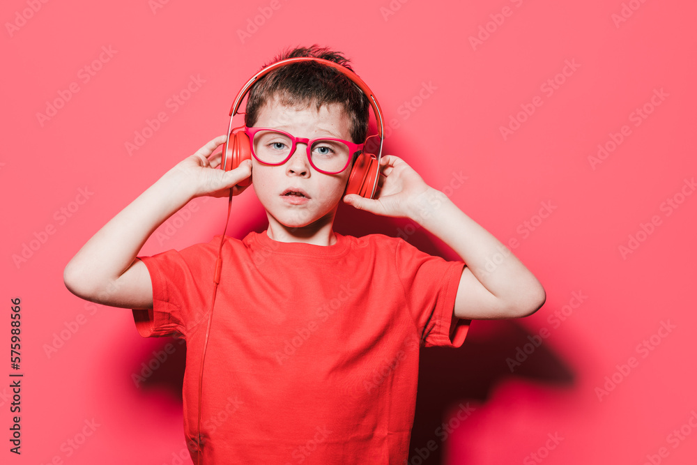 Kid adjusting headphones while standing against red background Kid adjusting headphones while standing against red background