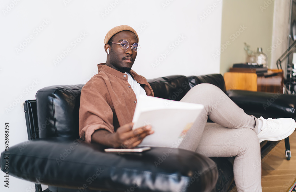 Serious black man resting on sofa with book in hand Serious black man resting on sofa with book in hand