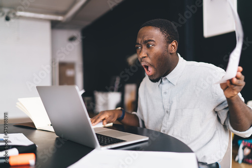 Amused black man working on computer in workspace