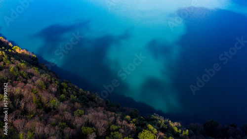 Aerial view of Lake Albano, a volcanic crater lake. A luxuriant forest grows around the water, which turns yellow and red in autumn.