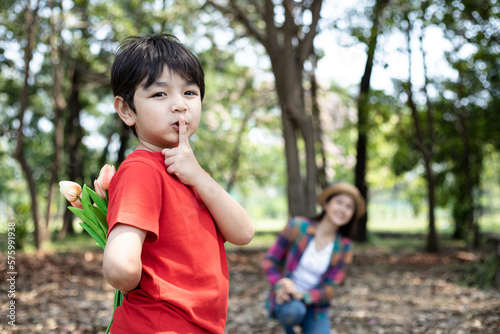 Children's date, boy hides flowers from a mother. Boy holds flowers behind his back and congratulates his mother at park. Secret concept.