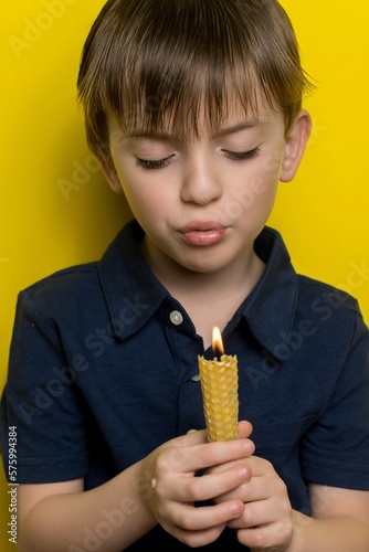 a little boy holds a beeswax candle in his hands. vertical photo