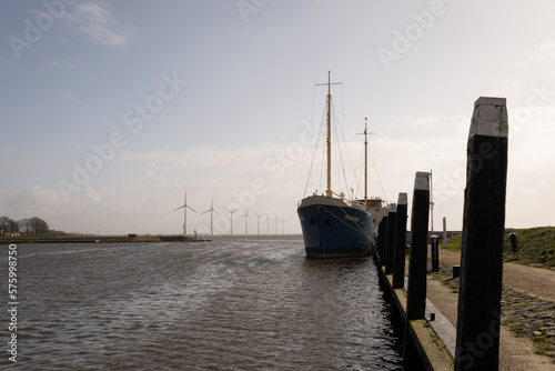 pleasure craft ship Pavona in Urk sea harbour with horizontal axis wind farm turbines in the background. The vessel in Dutch marina looks like a fishing trawler moored on the dockside.   photo