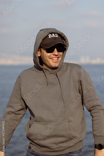 Young man in front of sea with sunglasses and hat written dad on it. He is alone. © burhan