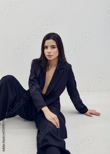 a beautiful woman poses relaxed sitting in a black suit on a light background