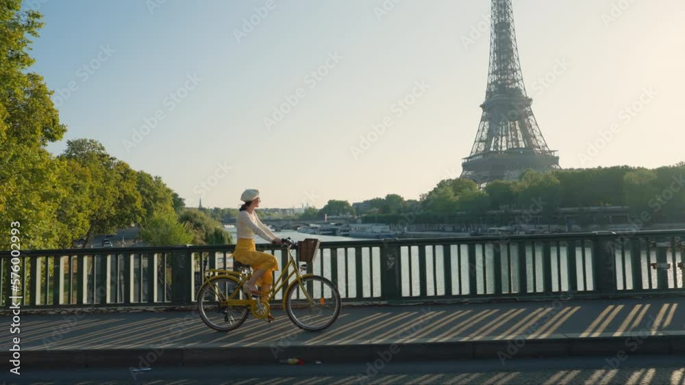Pretty woman riding a yellow bicycle on a bridge overlooking the Eiffel Tower