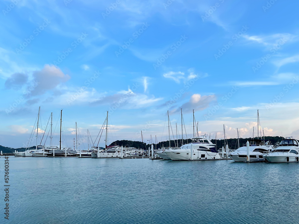View from the sea to the yachts anchored in the harbor. Lowered sails, empty masts are directed to the sky. Sailboats in the marina. Yachting and sailing. Ocean navigation season. Beautiful sunset