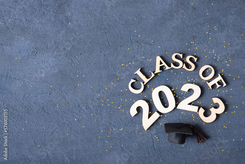Class of 2023 concept. Wooden number 2023 with graduate statuette on concrete background with tinsel top view