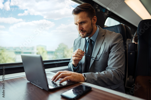 Handsome middle age businessman using his laptop computer while traveling with high-speed train. Modern and fast travel concept. © Dusko