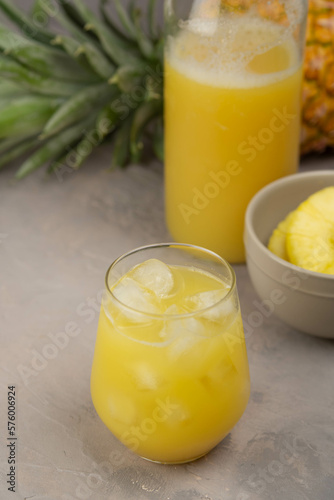 Pineapple juice in a clear glass and bottle on a light table. Pineapple and slices in the background.