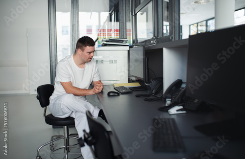 Young man with down syndrome working in hospital office, writing something on computer. Concept of integration people with disabilities into society.