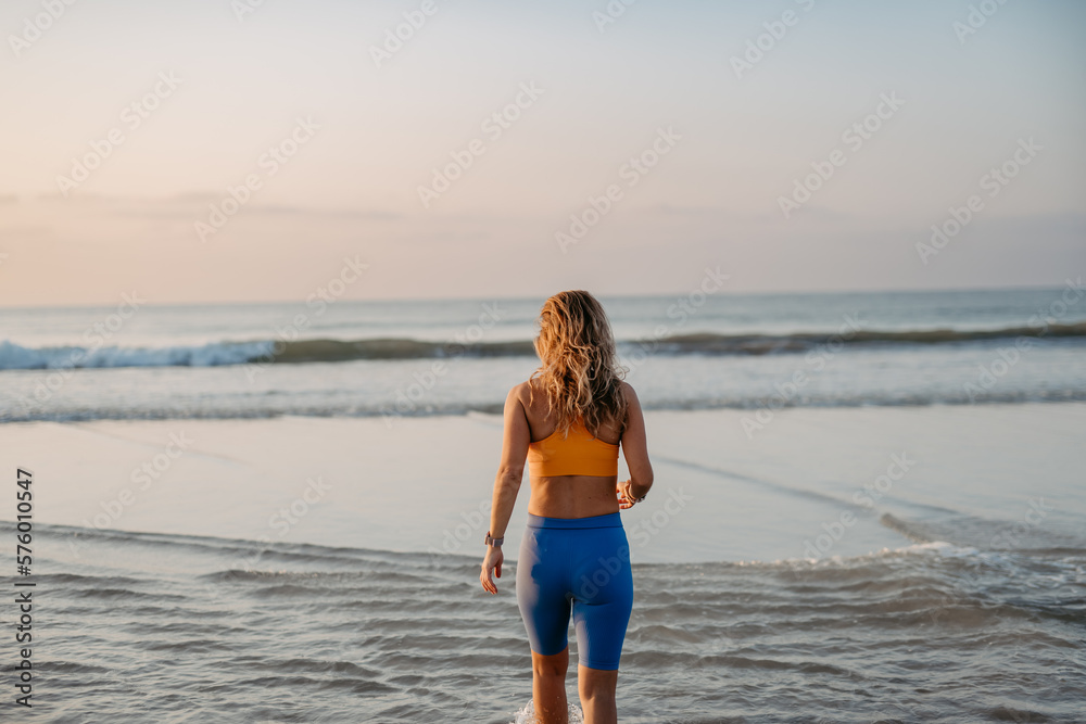 Rear view of young woman running on beach, morning routine and healthy lifestyle concept.