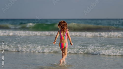 Little girl in swimsuit running in sea, enjoying holiday.