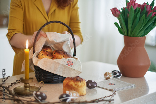 Woman with candle, preparing Easter basket with embroidered towel at kitchen home with tulips standing on the table. High quality photo
