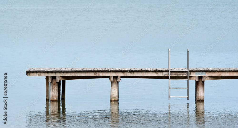 A jetty standing alone in a lake. Ladder for going down to the water. Calm water with no waves.

