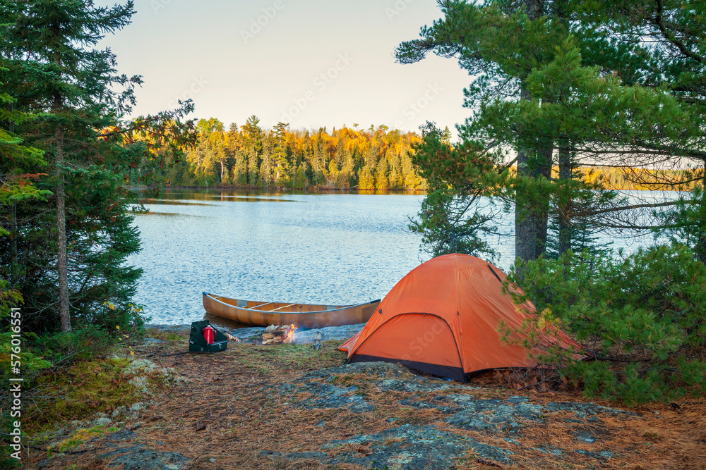 Campsite with orange tent and canoe on northern Minnesota lake at sunrise during autumn