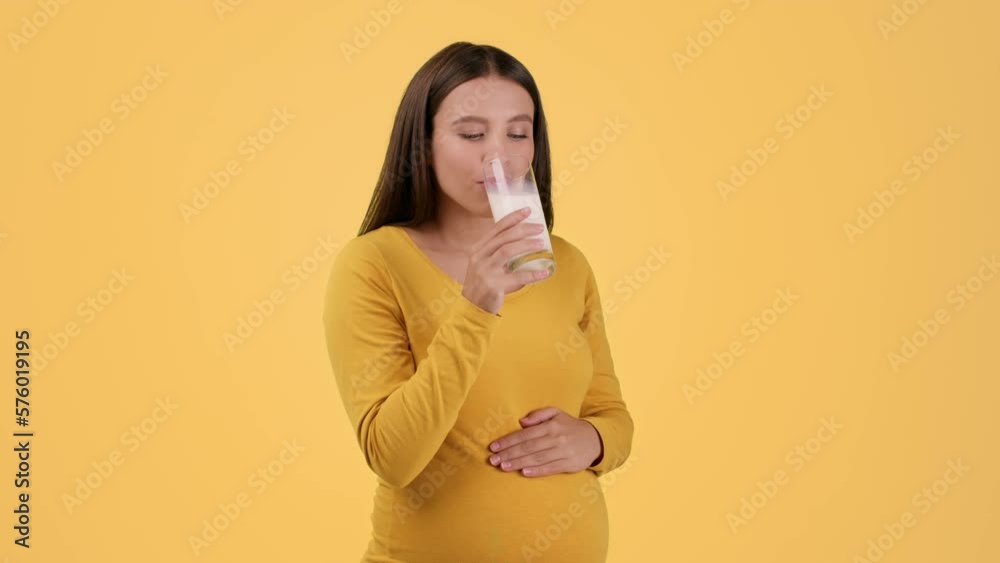 Calcium benefit. Young pretty pregnant woman enjoying glass of organic milk, licking her lips and smiling to camera