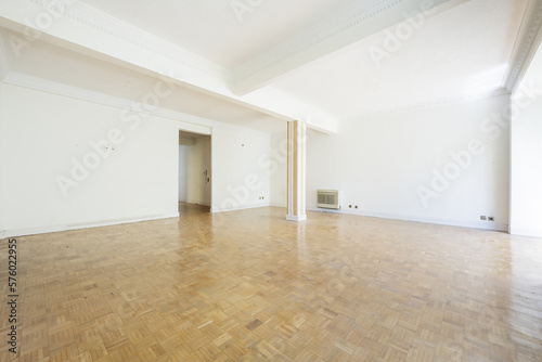 Living room of an empty house with parquet floors laid out in a checkerboard pattern with a painted pillar and access without a door