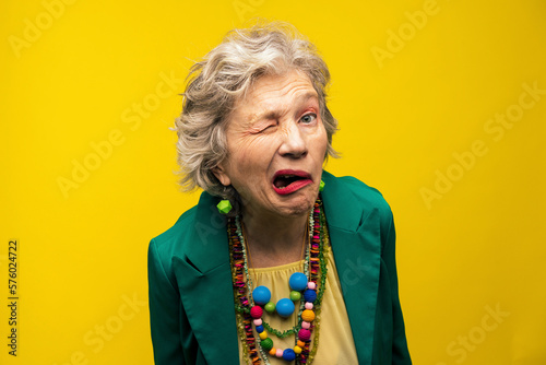 Senior woman making funny faces against yellow background photo