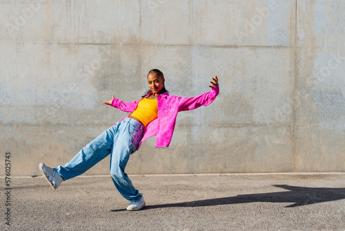 Smiling young woman dancing in front of wall