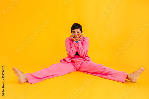 Happy young woman sitting with legs apart in over yellow background
