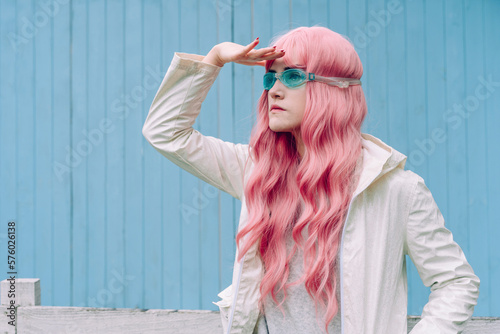 Young woman with pink hair searching in front of blue wall photo
