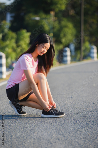 Close up of female runner kneeling and tying shoelace on the street. Fitness woman tying shoelaces. Young woman runner tying shoelaces in park with sunset and sunbeam.