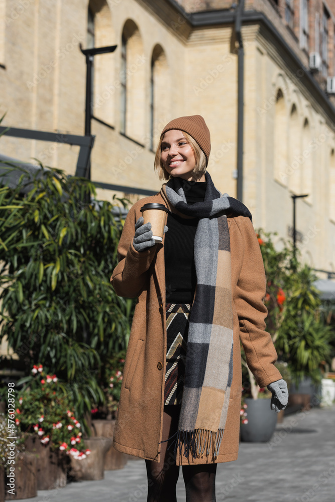 smiling young woman in stylish coat and beige hat holding paper cup with coffee to go. smiling young woman in stylish coat and beige hat holding paper cup with coffee to go.
