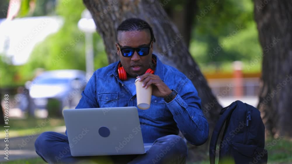 Modern entrepreneur works online from anywhere with a laptop and the internet. A dark-skinned man in dark glasses drinks a drink from a cup and processes orders in an online store Modern entrepreneur works online from anywhere with a laptop and the internet. A dark-skinned man in dark glasses drinks a drink from a cup and processes orders in an online store