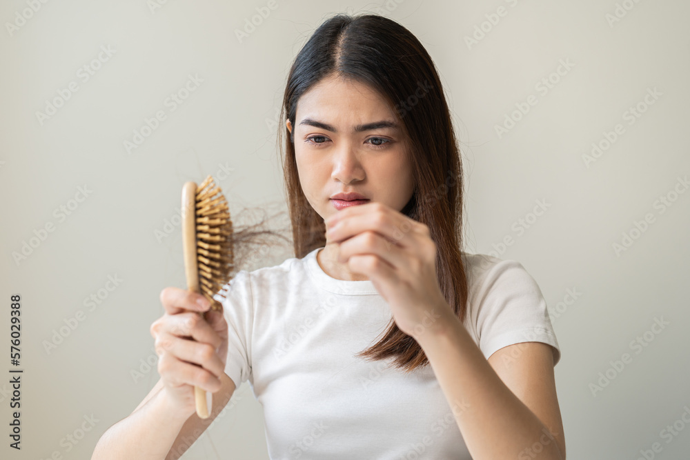 Serious asian young woman holding brush holding comb, hairbrush with fall black hair from scalp after brushing, looking on hand worry about balding. Health care, beauty treatment, hair loss problem. Serious asian young woman holding brush holding comb, hairbrush with fall black hair from scalp after brushing, looking on hand worry about balding. Health care, beauty treatment, hair loss problem.