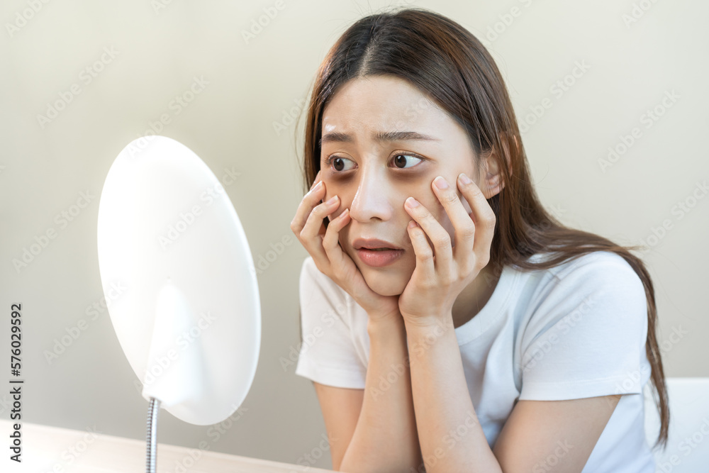 Bored, insomnia asian young woman, girl looking at mirror hand touching under eyes with problem of black circles or panda puffy, swollen and wrinkle on face. Sleepless, sleepy healthcare person. Bored, insomnia asian young woman, girl looking at mirror hand touching under eyes with problem of black circles or panda puffy, swollen and wrinkle on face. Sleepless, sleepy healthcare person.