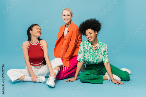 full length of cheerful multiethnic women in stylish casual attire posing on blue background.