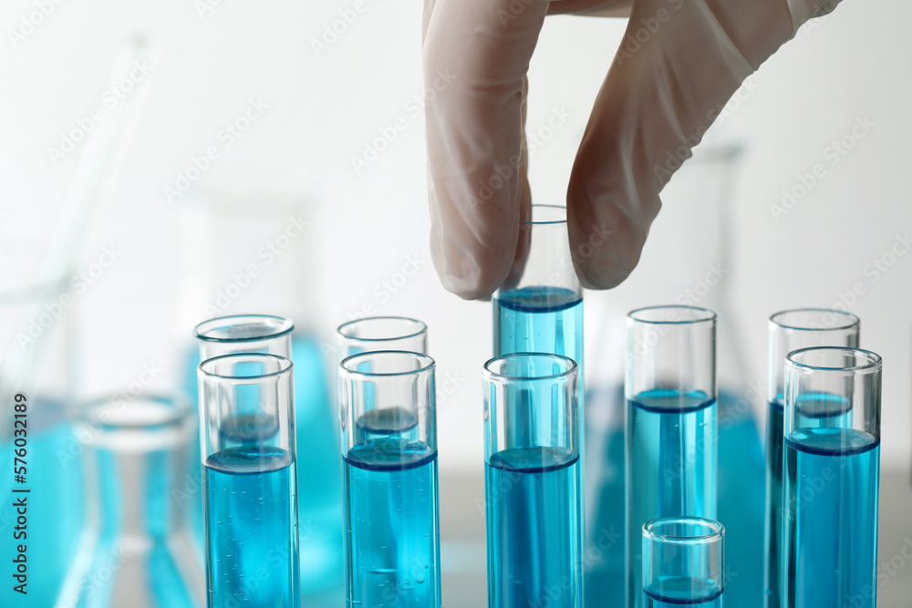 Scientist taking test tube with light blue liquid in laboratory, closeup Scientist taking test tube with light blue liquid in laboratory, closeup
