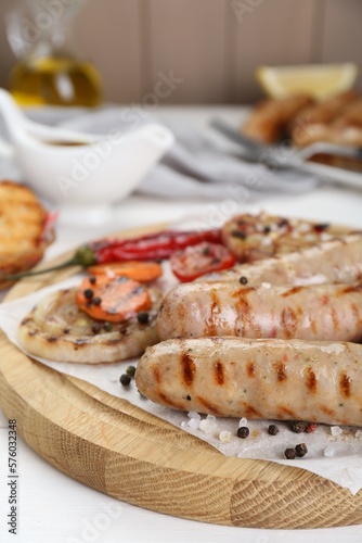 Tasty grilled sausages with vegetables and spices on white wooden table, closeup