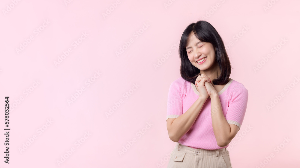 Adorable young happy asian woman model with shy emotion smiling expression cheerful positive attractive face and holding hand isolated on pink pastel studio background. Portrait beautiful cute lady. Adorable young happy asian woman model with shy emotion smiling expression cheerful positive attractive face and holding hand isolated on pink pastel studio background. Portrait beautiful cute lady.