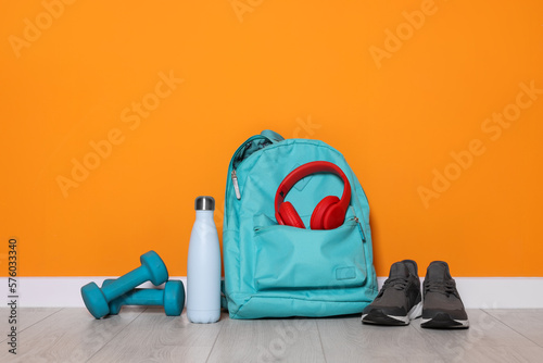 Backpack and sports equipment on floor near orange wall