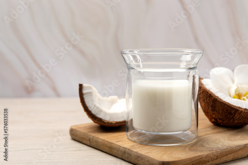 Glass of delicious vegan milk, coconut pieces and flower on white wooden table. Space for text