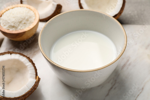 Bowl of delicious coconut milk  flakes and coconuts on white table