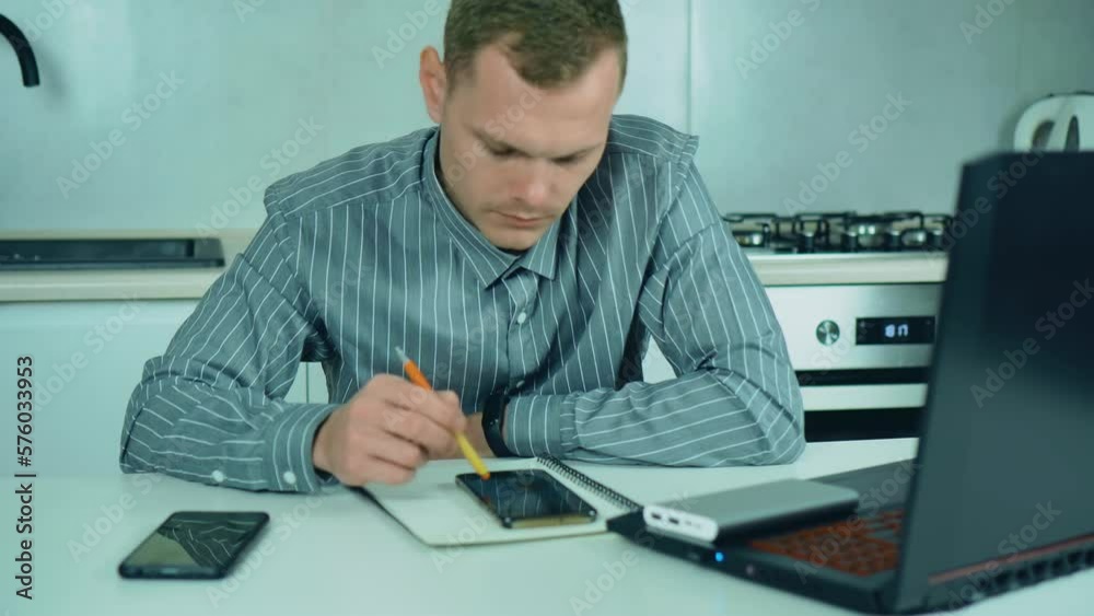 Blackout in Ukraine. Professional businessman with power bank searching electricity schedule for planning his work. Busy worker freelancer working at kitchen in financial sphere Blackout in Ukraine. Professional businessman with power bank searching electricity schedule for planning his work. Busy worker freelancer working at kitchen in financial sphere
