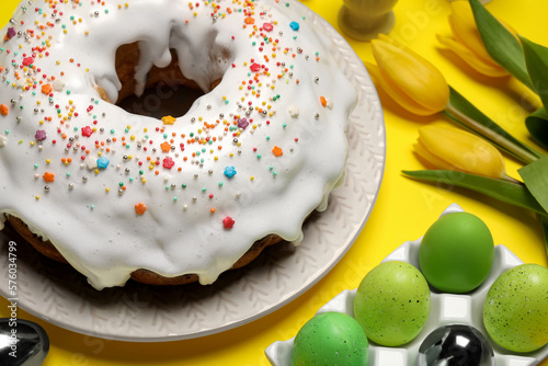Easter cake with sprinkles, painted eggs and tulips on yellow background