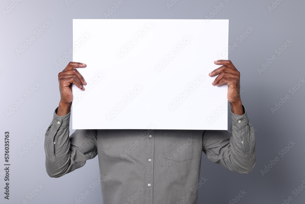 African American man holding sheet of paper on grey background, closeup. Mockup for design African American man holding sheet of paper on grey background, closeup. Mockup for design