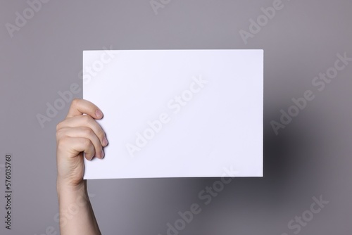 Woman holding sheet of paper on grey background, closeup. Mockup for design